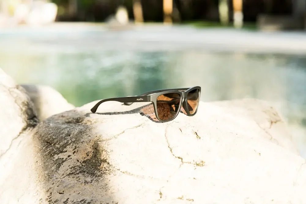 Polarised black sunglasses with UV protection on a sunlit rock by a pool