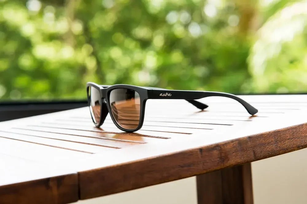 Polarised black sunglasses with brown lenses on wooden table, outdoor green background