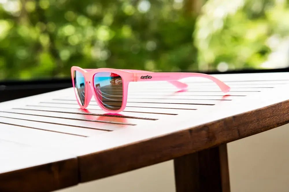 Pink polarized sunglasses with mirrored lenses on a wooden table outdoors