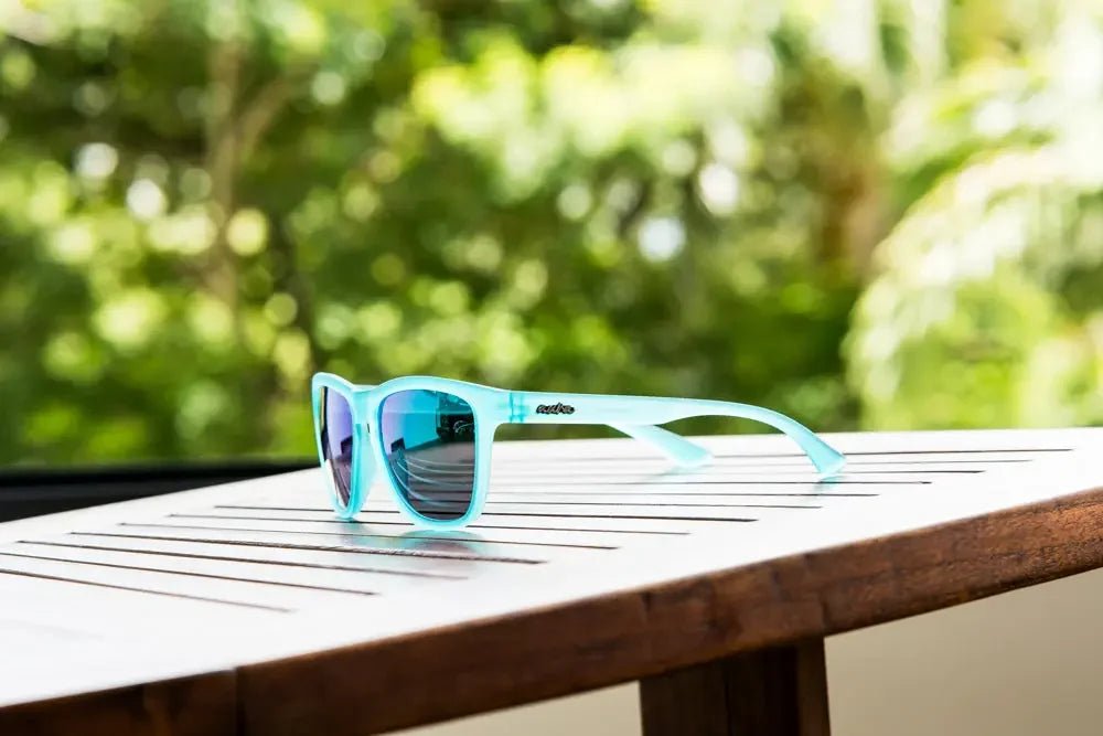 Blue polarized sunglasses with mirrored lenses on outdoor wooden table, green background
