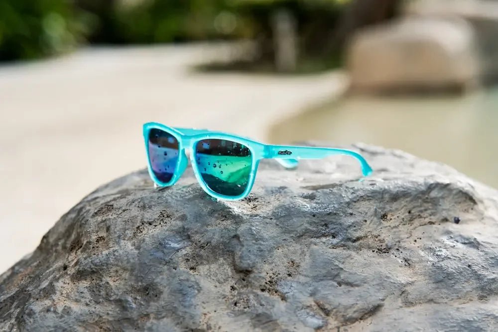 Blue polarized sunglasses with mirrored lenses on a rock by water outdoors