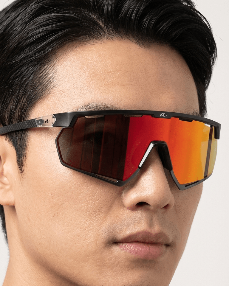 Person wearing a pair of sunglasses with a reflective red lens on a neutral background